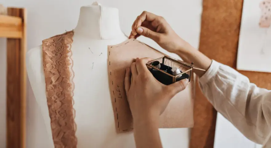 Mani che lavorano su un manichino, creando un modello di cartone. Un corso di modellistica in pieno svolgimento, con pizzi e accessori da cucito a portata di mano.