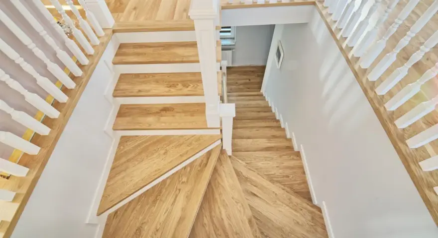Eleganckie schody angielskie z drewna dębowego, z białymi balustradami, prowadzą w dół.