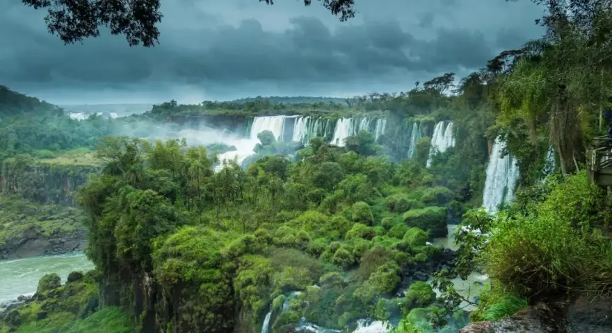 Majestuosas cataratas del Iguazú, un torrente de agua cayendo entre exuberante vegetación bajo un cielo nublado.