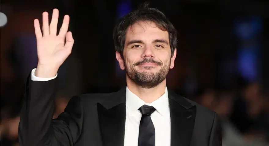 Valerio Vestoso saluta con la mano, sorridendo con un abito elegante.