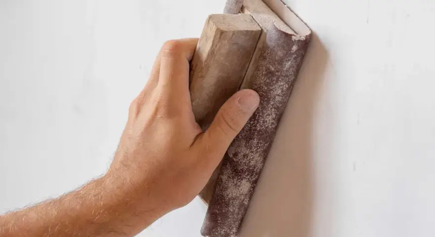 Mano lijando una pared con lija para pared y bloque de madera.