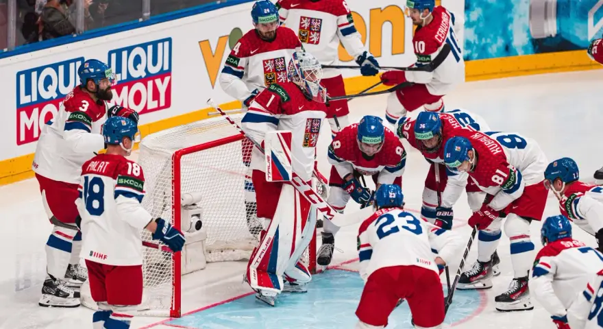 Czescy hokeiści w akcji podczas mistrzostw świata w hokeju 2024. Drużyna w białych strojach z czerwonymi i niebieskimi elementami walczy o zwycięstwo.