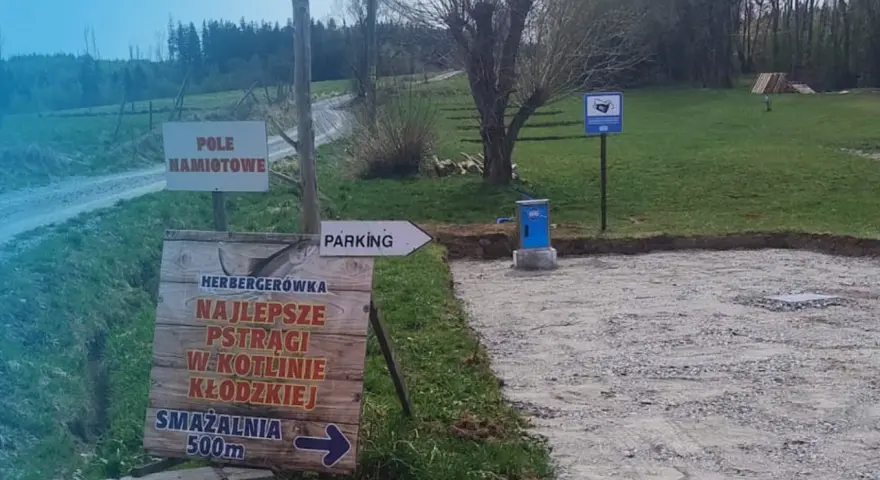 Miejsce na parking dla kamperów. Obok znak "Pole Namiotowe" i drogowskaz do smażalni pstrągów.