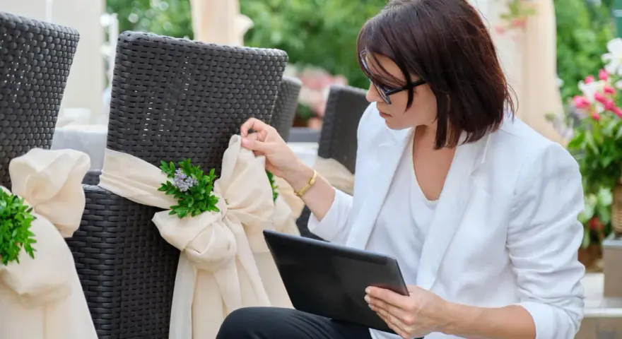 Kobieta w białej marynarce dopina wstążkę na krześle. Czy warto wynająć wedding plannera na samą koordynację dnia ślubu?