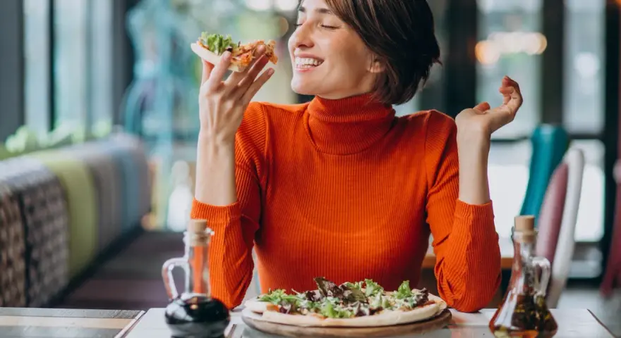 Kobieta w pomarańczowym golfie cieszy się pizzą, czując radość. W czym jest serotonina? W takich chwilach szczęścia!