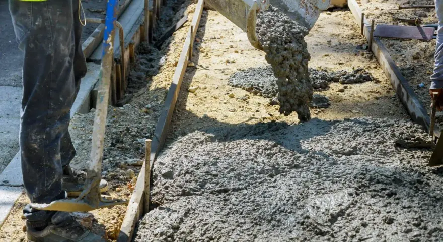 Beton wylewany z gruszki na plac budowy. Pracownik przygotowuje teren pod wylanie betonu.