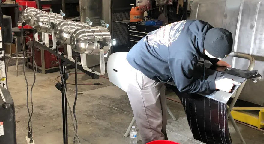 A person in a garage works on a car part, learning how to buff it to a shine.