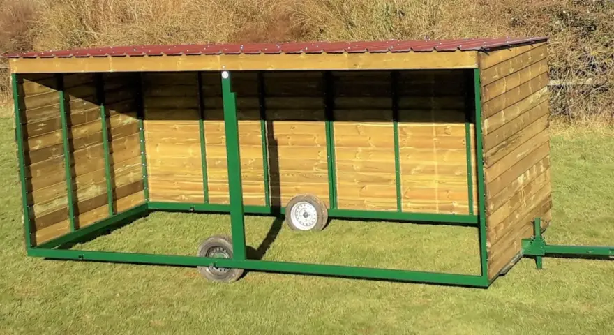 Abri pour chevaux en bois, mobile et sans permis de construire, avec toit rouge et structure verte.