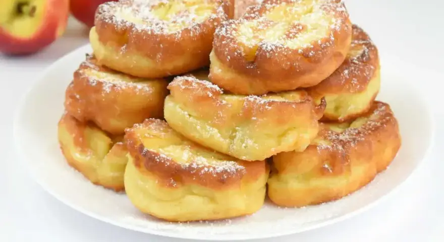 Puszyste racuchy na kefirze jak u babci, posypane cukrem pudrem, obok jabłka.