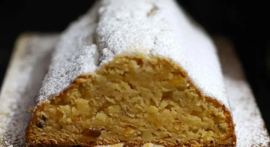 Ein saftiger Quarkstollen mit Marzipan, bestäubt mit Puderzucker, wartet auf den Anschnitt.