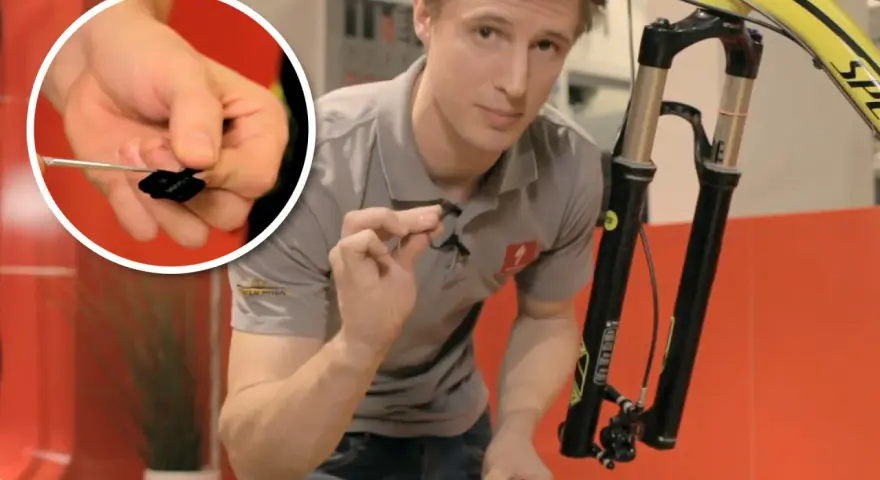 Man visar hur man byta bromsklossar på en cykel. En närbild visar en liten svart bromskloss.