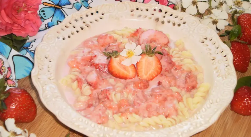 Makaron fusilli z sosem truskawkowym, udekorowany połówkami truskawek i kwiatkiem.