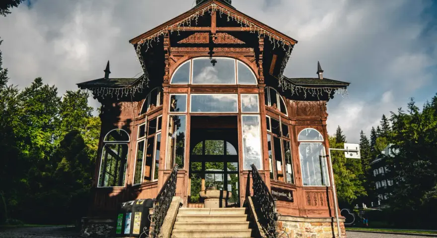 Drewniany pawilon w Karlovej Studance, ozdobiony lampkami, zaprasza do środka. Wspaniała architektura i otoczenie lasu tworzą magiczną atmosferę.