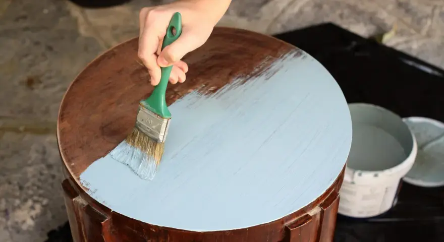Mano aplicando pintura a la tiza color madera a una mesa redonda.