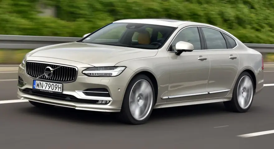 Eleganckie Volvo S90 w kolorze szampańskim pędzi po drodze. Choć piękny, warto pamiętać o potencjalnych wadach tego modelu.