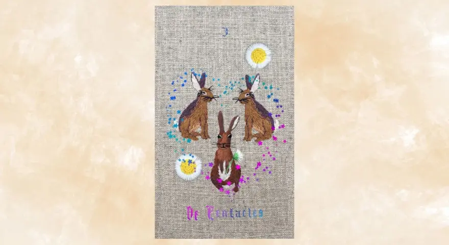 Tres conejos bordados, uno en el centro y dos a los lados, rodeados de flores y confeti. El número 3 y "De Pentaculos" escritos.