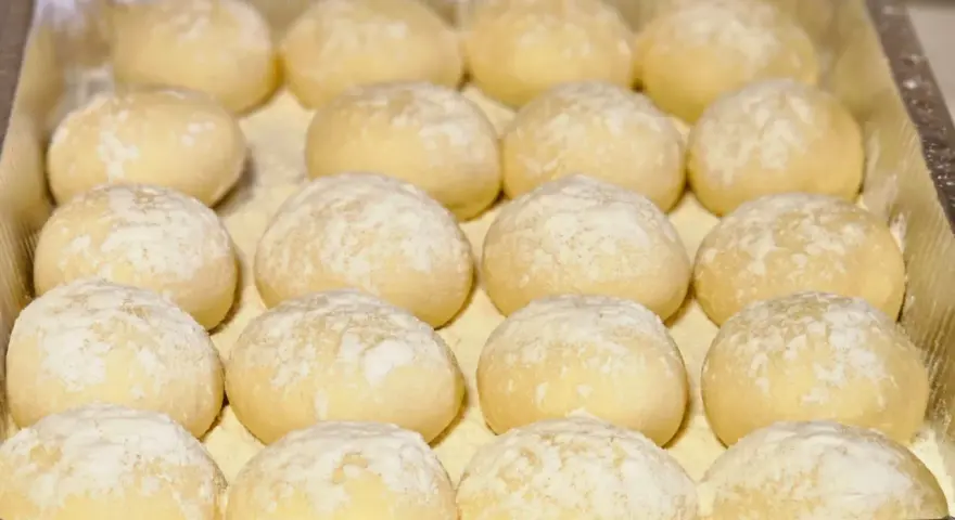 Piccolo pane fatto in casa, soffice e leggermente infarinato, pronto per essere infornato.