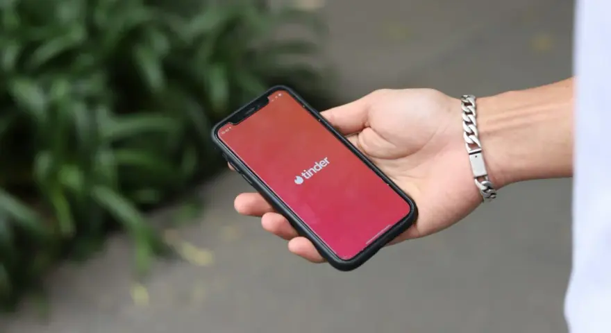 Dłoń trzyma smartfon z otwartą aplikacją Tinder. Zastanawiasz się, jak znaleźć osobę z Tindera na Facebooku?