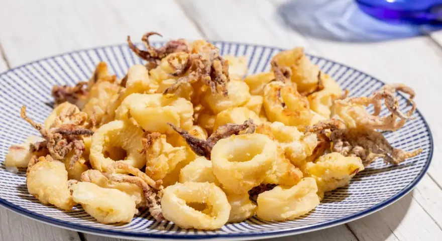Calamari croccanti e dorati, cotti alla perfezione nella friggitrice ad aria, serviti su un piatto a righe blu.