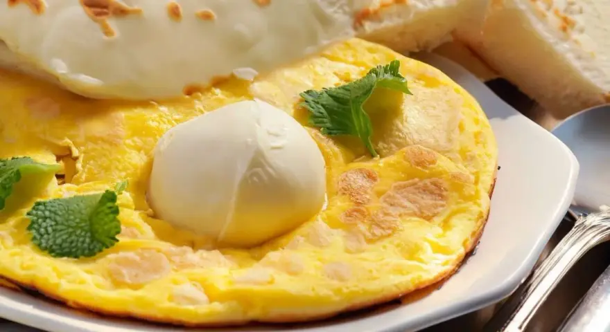 Frittata soffice con mozzarella filante, guarnita con foglie di menta fresca. Accompagnata da fette di pane tostato.