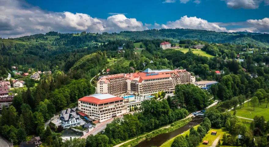 Widok z lotu ptaka na duży hotel Gołębiewski otoczony zielonymi wzgórzami i rzeką.