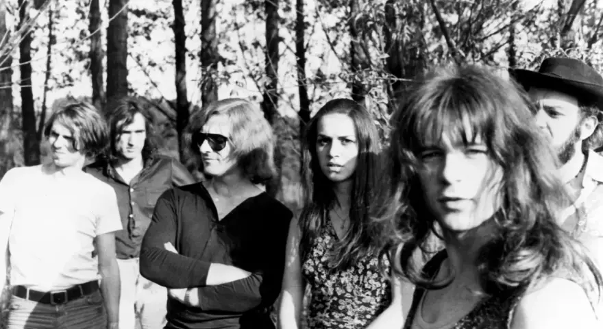 Un groupe rock allemand des années 70, avec des membres aux cheveux longs et des tenues décontractées, posant devant des arbres.