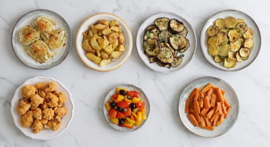 Sette piatti di verdure in friggitrice ad aria: finocchi, patate, melanzane, zucchine, cavolfiore, peperoni e carote.