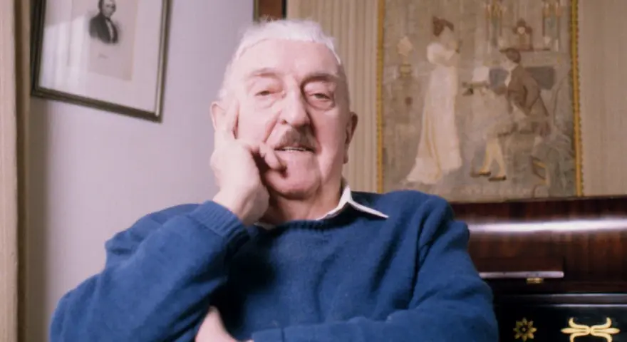 Jerzy Waldorff, znany z zamiłowania do kultury i sztuki, w niebieskim swetrze. Jego wykształcenie i pasje widoczne w tle.