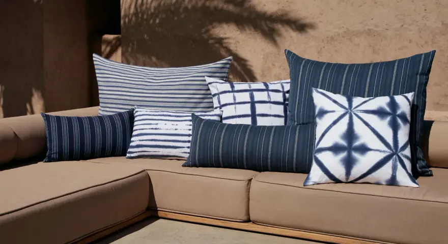 Idée déco plaid sur canapé : coussins bleus et blancs aux motifs rayés et tie-dye sur un canapé de jardin.