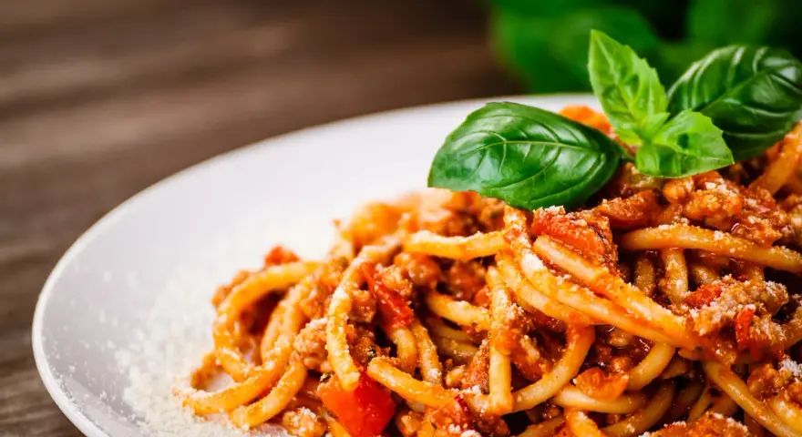 Pyszne spaghetti bolognese, idealne na prosty przepis. Danie ozdobione świeżą bazylią i startym parmezanem.