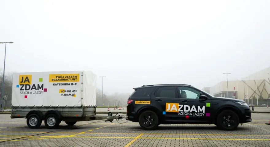 Czarny SUV z przyczepą szkoleniową "JA ZDAM" na placu manewrowym. Zestaw do kategorii B+E gotowy do egzaminu.