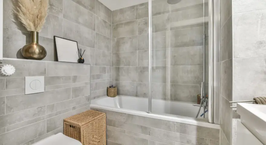 Salle de bain moderne avec carrelage gris. Une baignoire, une douche, un WC et un lavabo. Quelle colle pour carrelage salle de bain ? Une colle adaptée à l'humidité est essentielle.