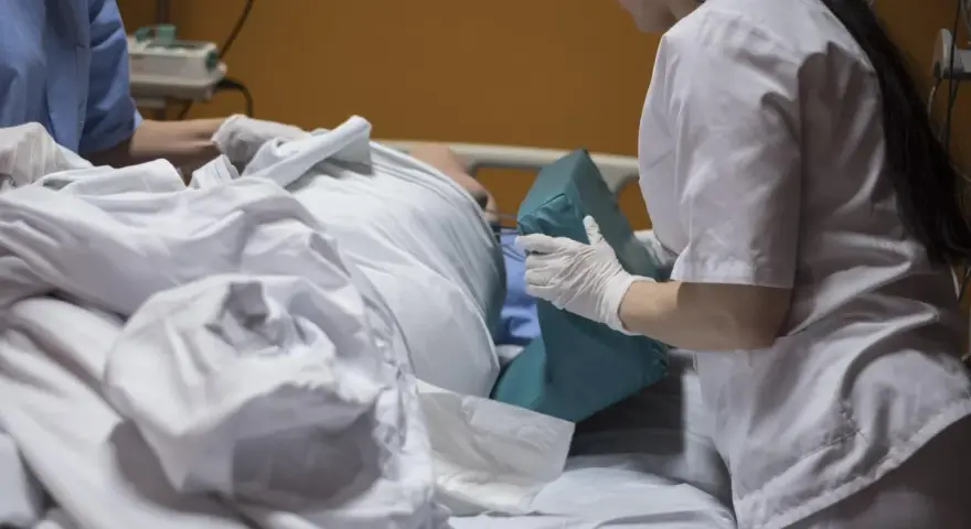 Asystent pielęgniarki, wykonując swoje uprawnienia, pomaga pacjentowi w łóżku, podkładając poduszkę.