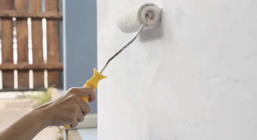 Mano aplica capa de imprimación blanca a una pared con un rodillo de pintura amarillo.