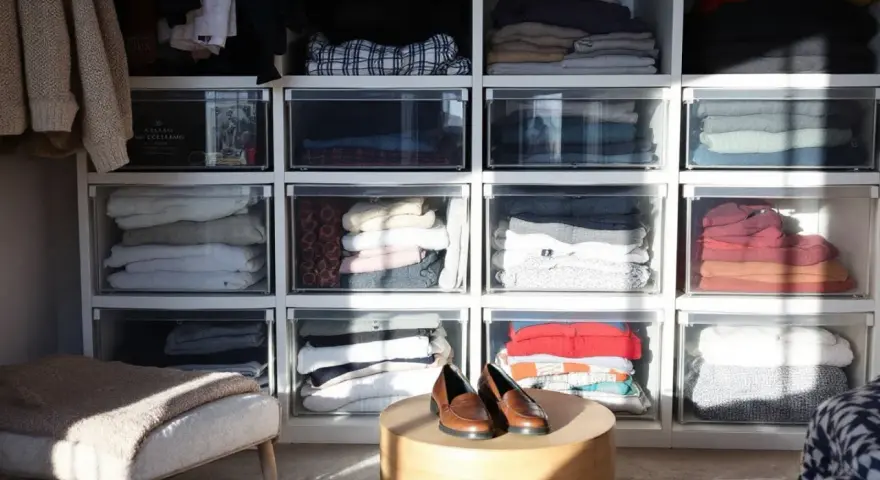 Des vêtements pliés dans des tiroirs transparents, une solution pour optimiser rangement vetements. Des chaussures marron sur une table basse.