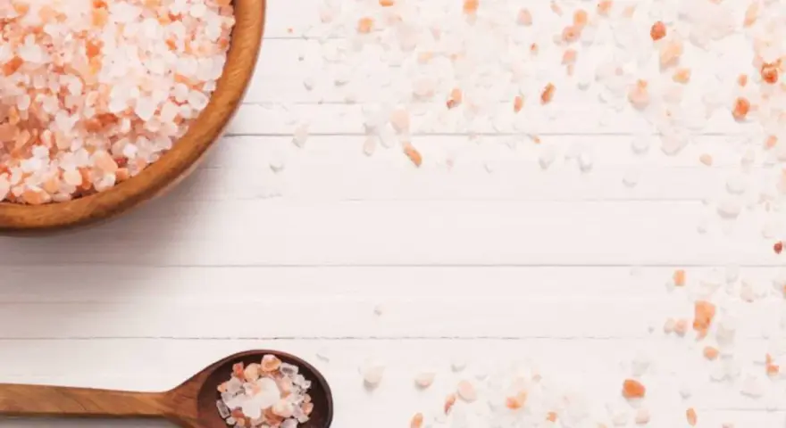 Sal del Himalaya en cuenco de madera y cuchara, mostrando sus propiedades y color rosado natural.