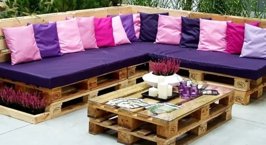Narożna sofa i stolik kawowy z palet, ozdobione kolorowymi poduszkami i wrzosem. Prawdziwe cuda z palet!