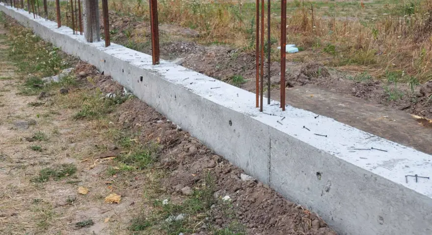 Zbrojony fundament czeka na wylewanie betonu. Widać stalowe pręty wystające z betonowej ławy fundamentowej.