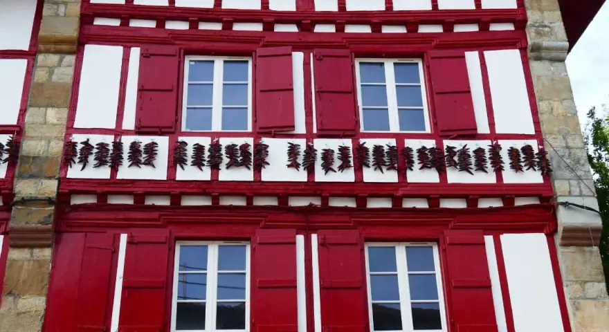 Façade rouge et blanche typique d'Espelette, avec des piments séchant. Combien de temps pour visiter Espelette ? Une journée suffit pour admirer ce village pittoresque.