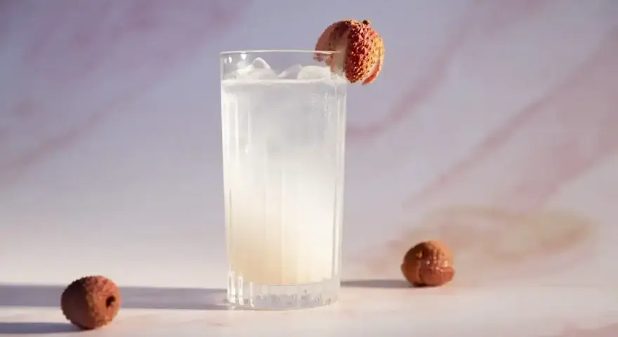 Orzeźwiający drink z liczi, ozdobiony owocem, z dwoma całymi liczi obok. Idealny na letnie popołudnie.