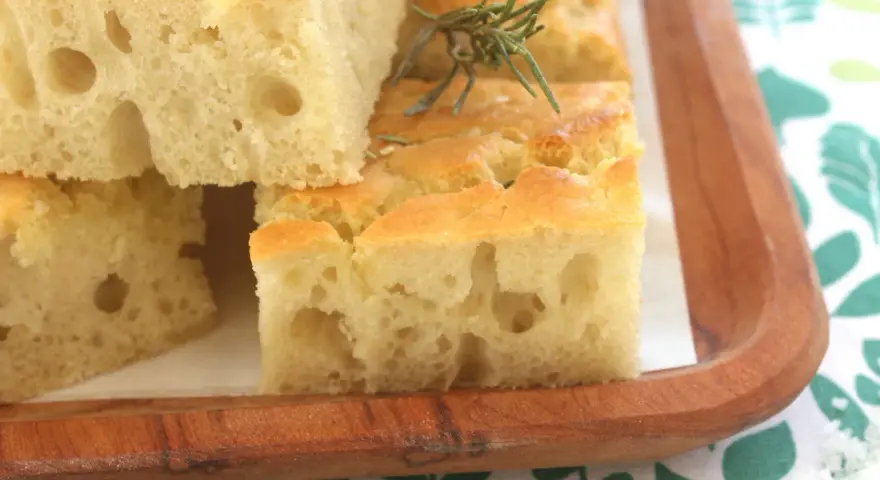 Focaccia alta e soffice, tagliata a cubetti, guarnita con rosmarino e sale grosso, servita su un tagliere di legno.