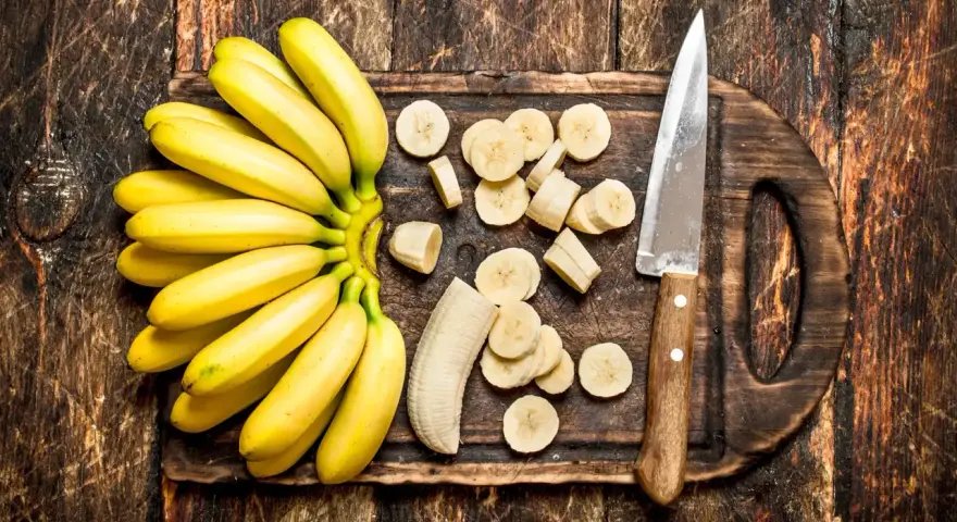 Pęczek żółtych bananów i pokrojone plasterki na desce. Dowiedz się, jak przechowywać banany, by dłużej były świeże.
