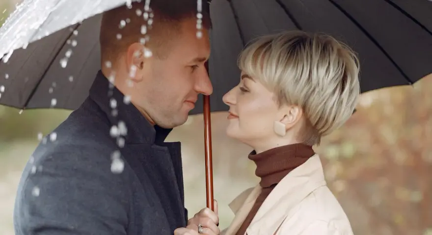 Para w deszczu pod parasolem. Młodszy partner patrzy z czułością na swoją ukochaną.