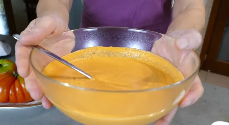 Mani che sorreggono una ciotola di vetro con una cremosa maionese di pomodoro, pronta per essere gustata.
