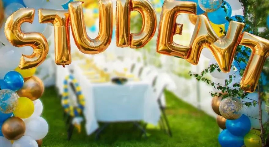 Gyllene folie ballonger bildar ordet "STUDENT" framför en festdukning utomhus.