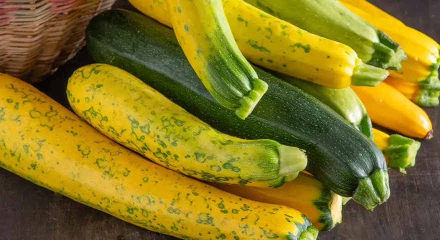 Frische, bunte Zucchini liegen neben einem Korb. Perfekt, um sie roh zu essen und den Sommer zu genießen.