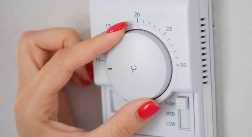 Dłoń z czerwonym lakierem reguluje termostat, ustawiając temperaturę dla elektro zaworów do CO.