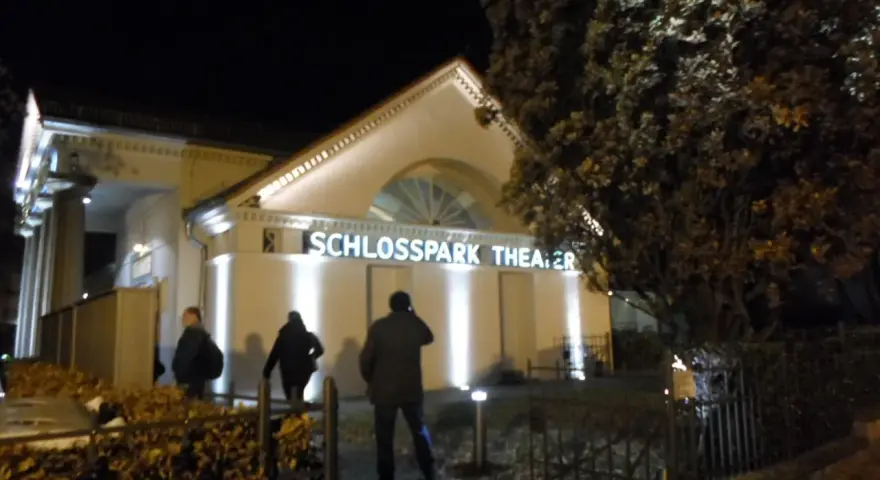 Abendliche Beleuchtung am **Schlosspark Theater**. Drei Personen nähern sich dem Eingang.