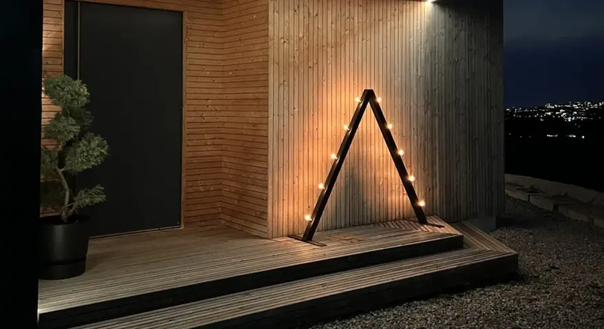 En triangulär ljusstake diy med glödlampor lyser upp entrén till ett modernt trähus.