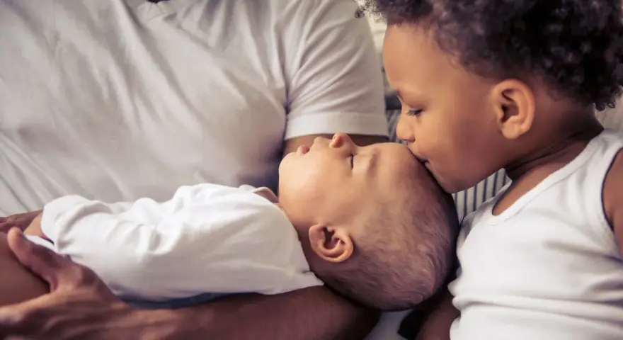 Ein älteres Kind küsst liebevoll die Stirn eines Babys. Die Frage "zweites Kind ja oder nein" scheint hier beantwortet.